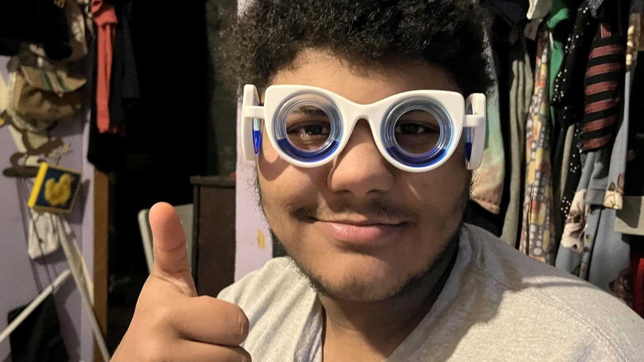 A young man wearing motion sickness glasses gives a thumbs up, smiling confidently.