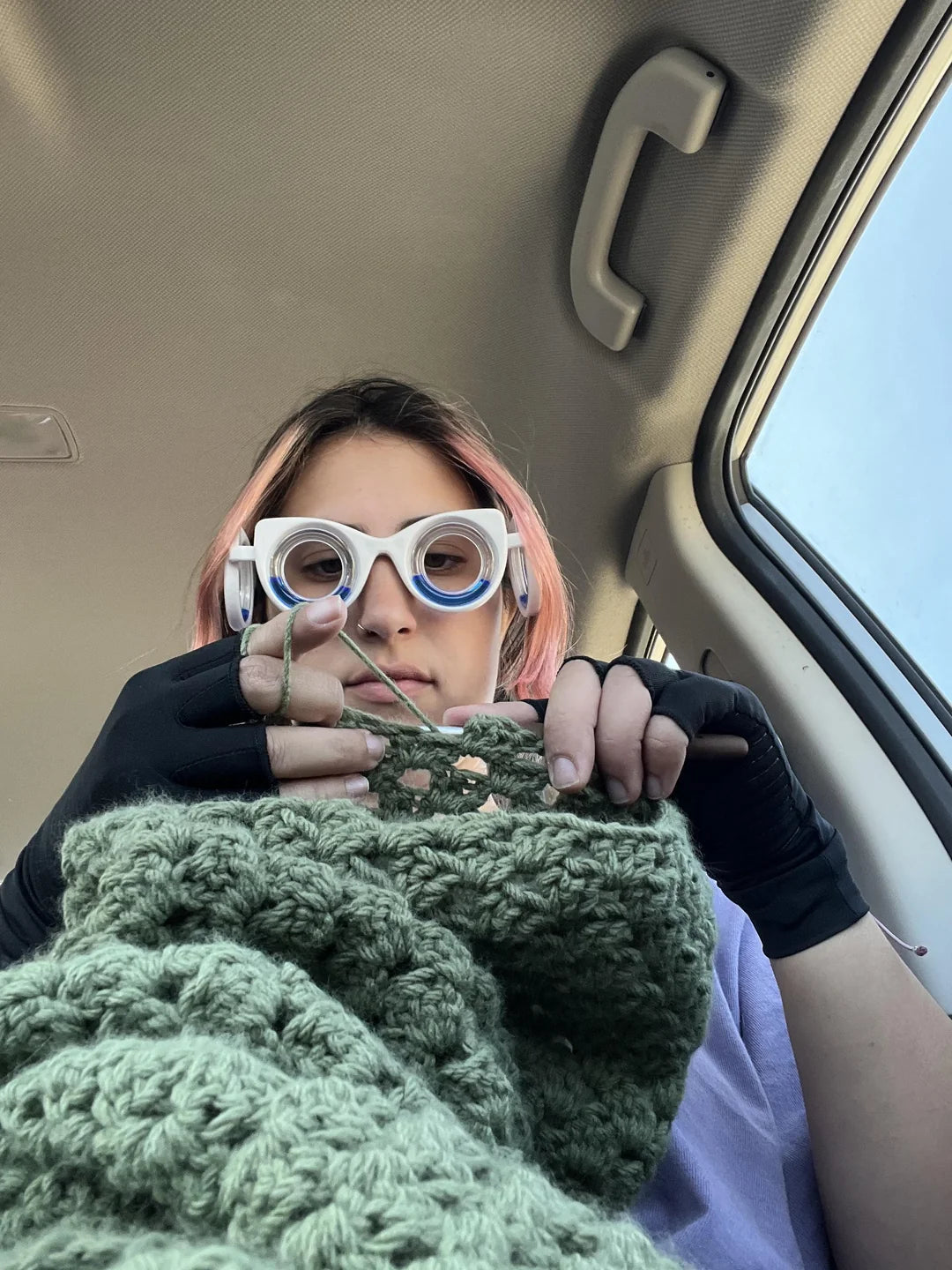 A woman wearing motion sickness glasses knitting a green sweater sitting in the car