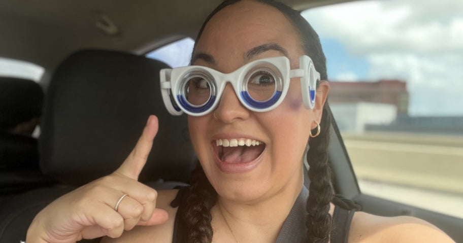 Happy woman sitting in the back seat of a car, wearing motion sickness glasses and gesturing excitedly with an open mouth, expressing enjoyment and relief from motion discomfort.