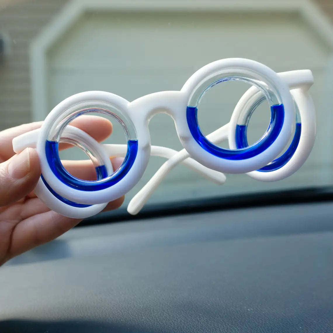 White motion sickness glasses, folded and held by hands inside a car, emphasizing convenience and portability for travel comfort.