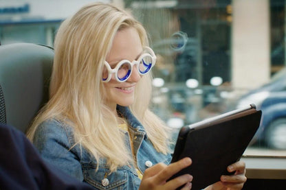 A woman wearing motion sickness glasses, holding a tablet, appears focused and engaged with her device, sitting in a vehicle.